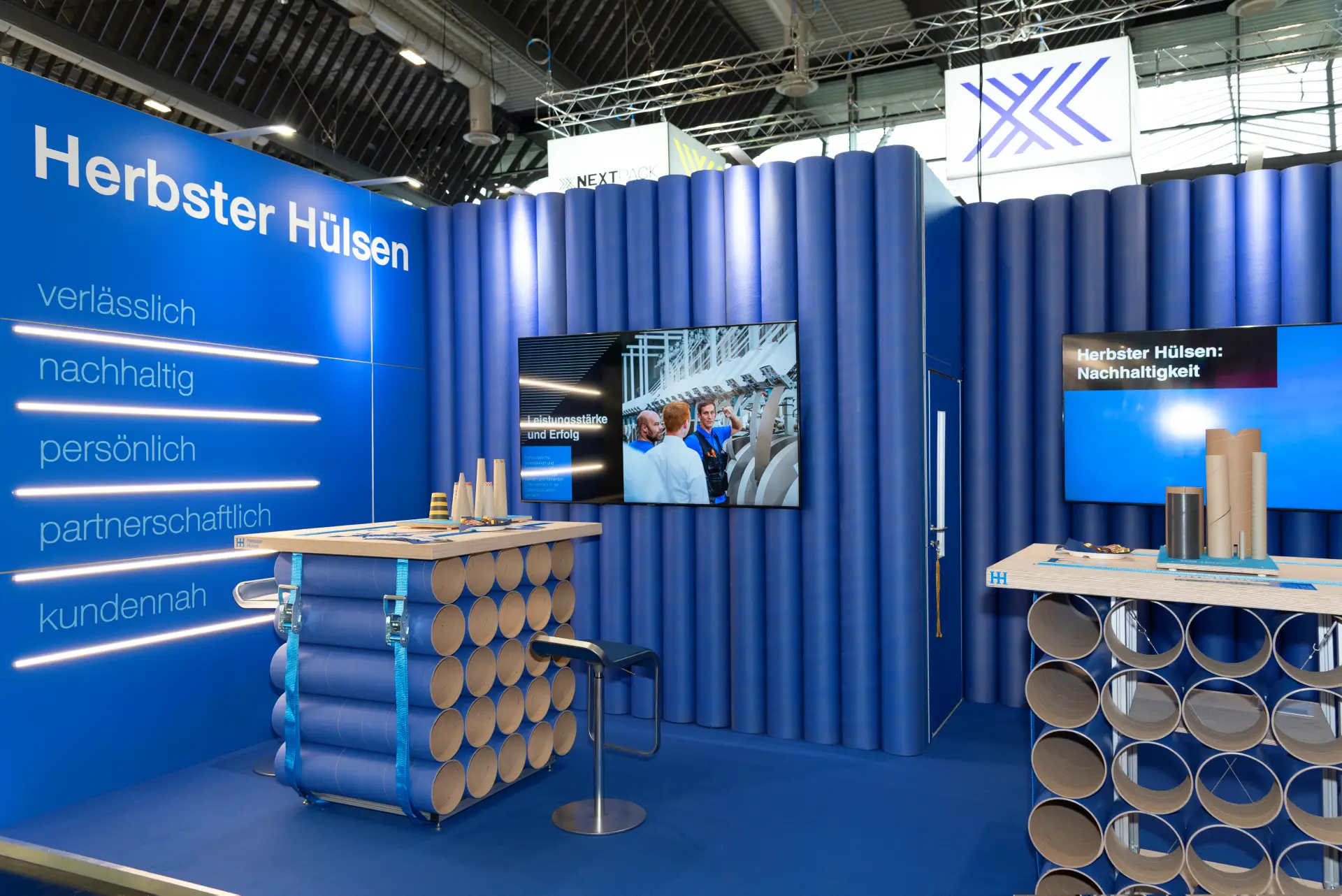 Blauer Messestand von Herbster Hülsen mit Markenbotschaften wie verlässlich, nachhaltig und partnerschaftlich auf der FachPack 2025 – professioneller Messebau Nürnberg.