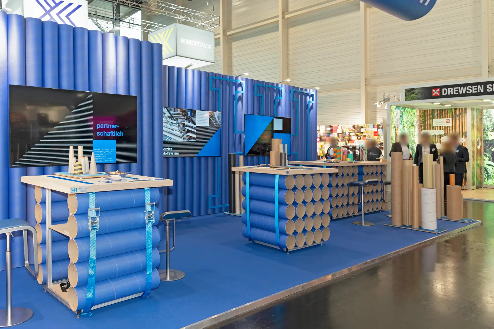 Moderner FachPack-Messestand von Herbster Hülsen mit blauen Hülsenmodulen, Präsentationsdisplays und nachhaltigen Materialien – innovativer Messebau Nürnberg.
