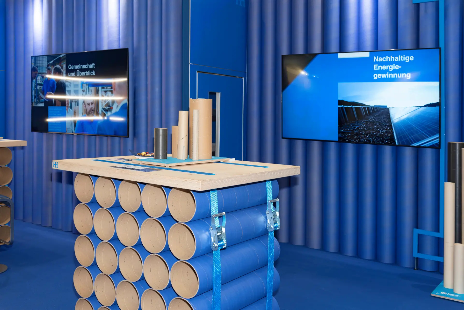 Großflächiger Messestand von Herbster Hülsen auf der FachPack 2025 in Nürnberg – nachhaltige Präsentation von Hülsenprodukten im blauen Markenlook – Messebau Nürnberg.