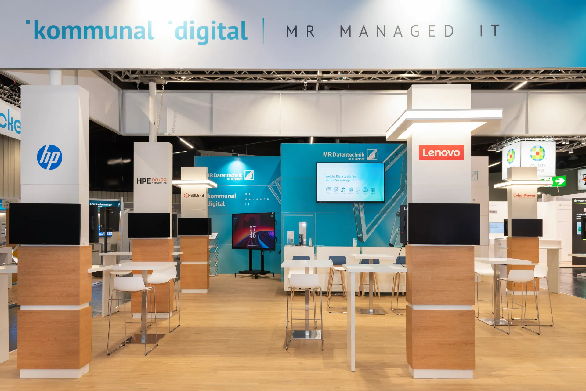 Frontansicht des MR-Datentechnik-Messestands in Nürnberg mit Schriftzug kommunal digital MR Managed IT, Holzelementen, Barhockern und Markenlogos HP, HPE, Lenovo und Kyocera.