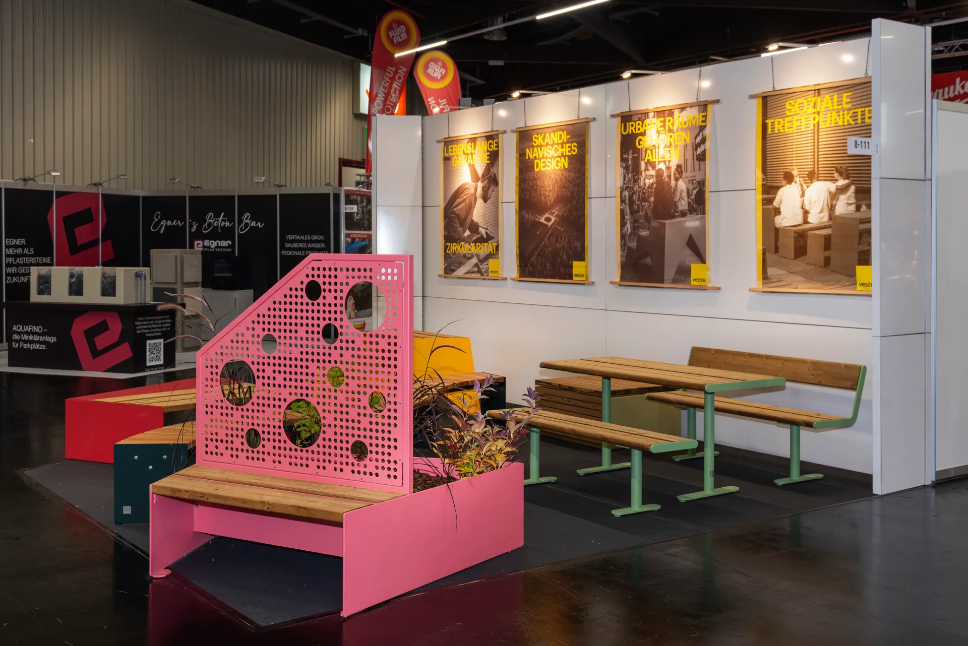 Vestre-Stand auf der Kommunalmesse Nürnberg mit pinkem Lochblech-Sitzelement und Bepflanzung, Holzbänken mit grünem Gestell und gelber Plakatwand