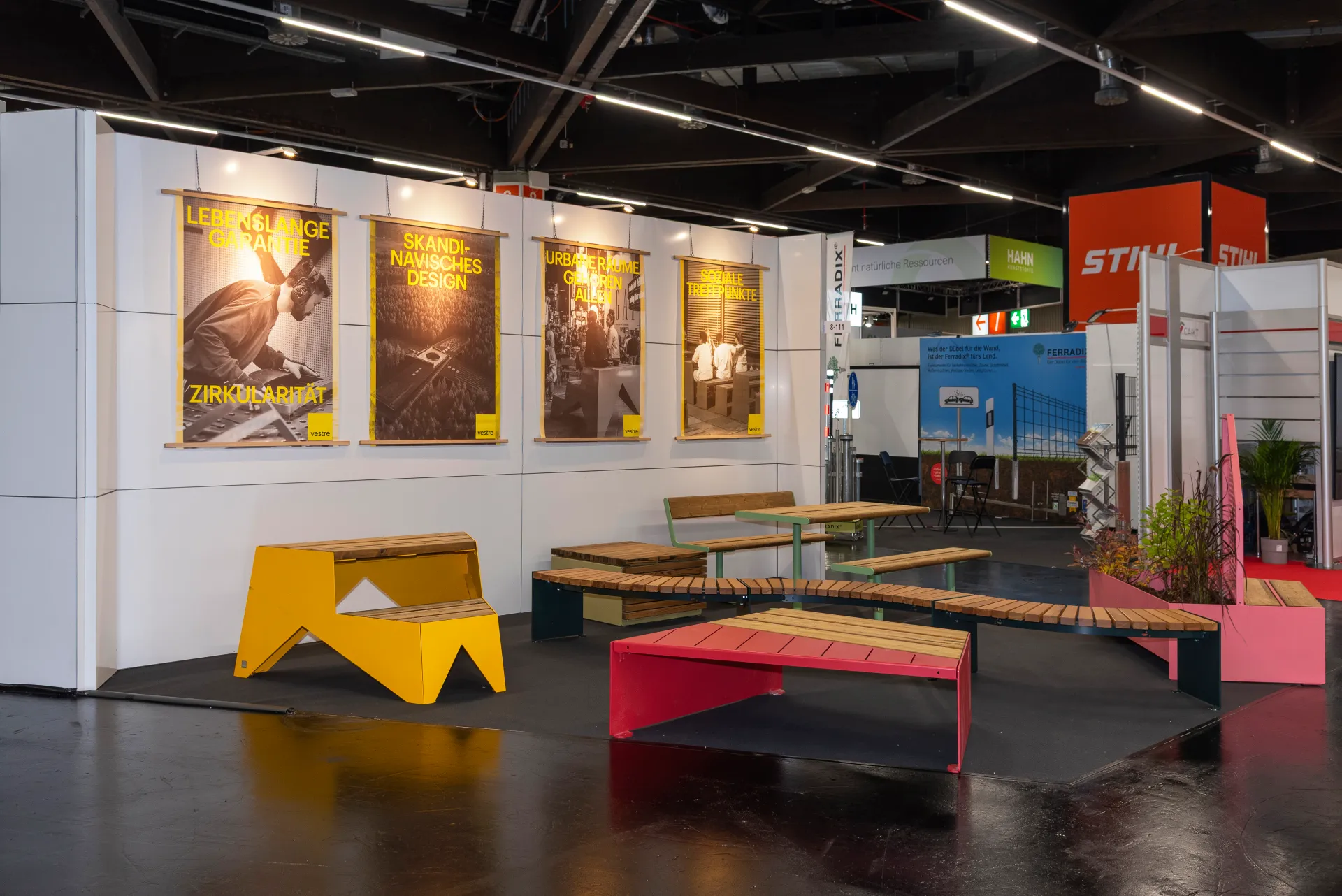 Vestre-Messestand in Nürnberg mit Holzbänken, gelben, roten und grünen Outdoor-Möbeln und gelber Plakatserie, im Hintergrund der STIHL-Stand