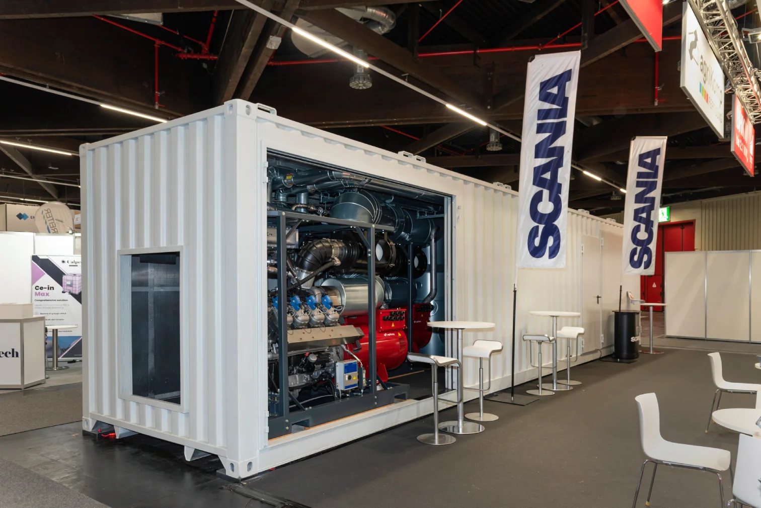 Geöffneter weißer Container am agriKomp-Messestand mit sichtbarem Biogas-BHKW-Motor und blauen Scania-Flaggen in einer Messehalle in Nürnberg.