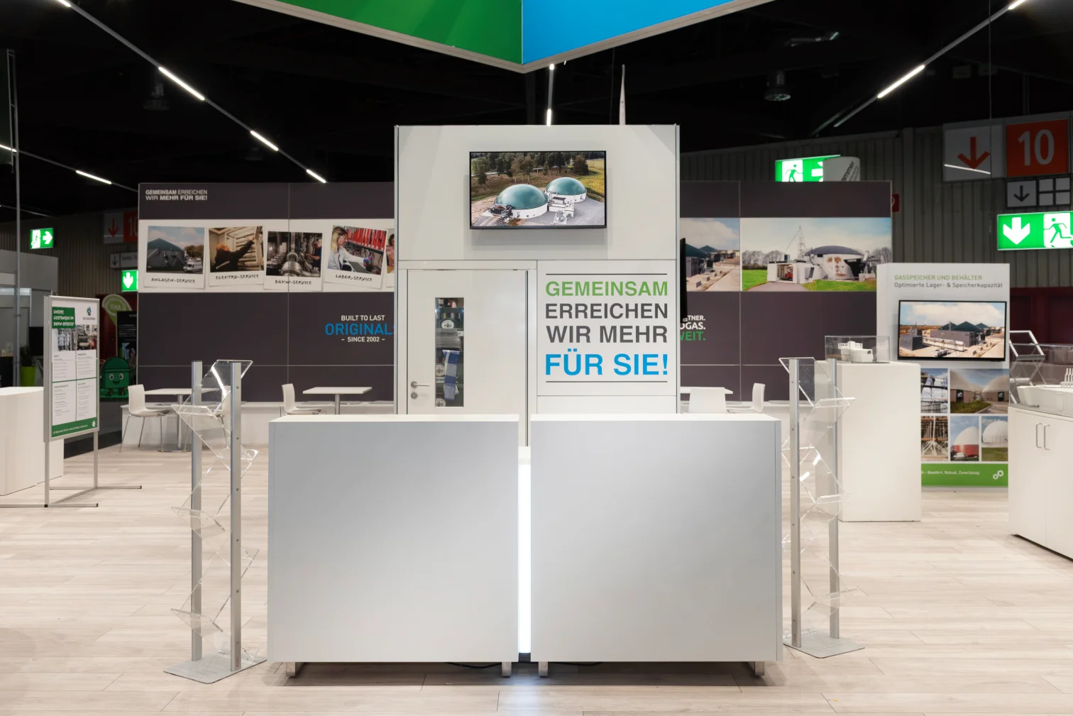 Empfangstheke des agriKomp-Messestands in Nürnberg mit Bildschirm, Slogan Gemeinsam erreichen wir mehr für Sie und umlaufender Biogas-Bildwand.