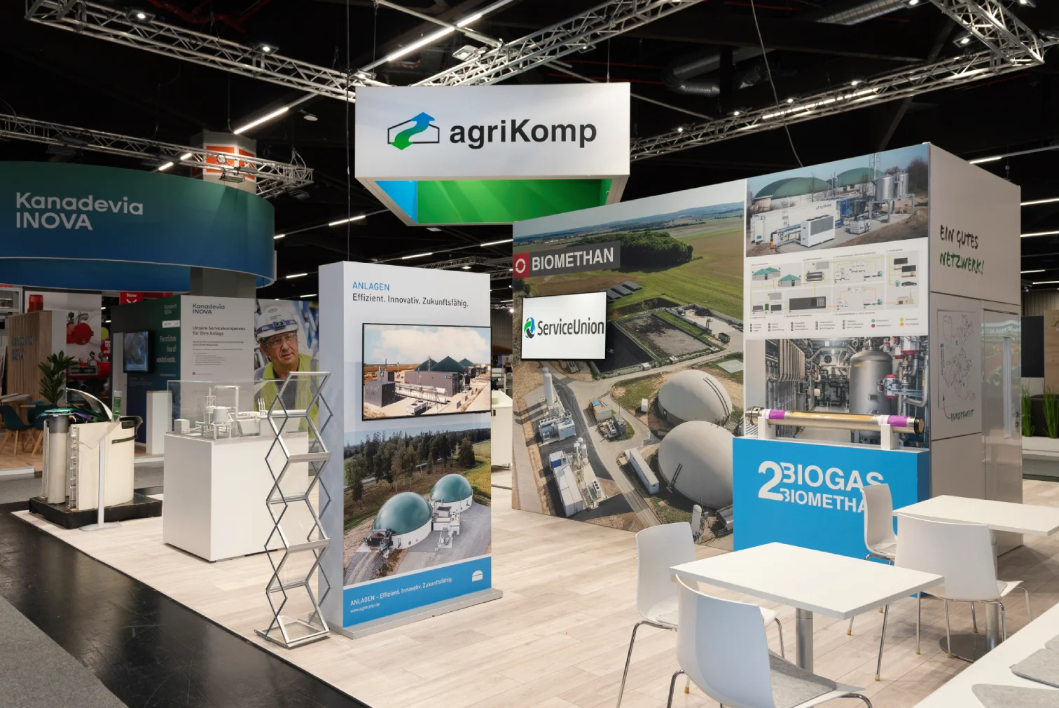 Messestand von agriKomp in Nürnberg mit grün-weißem Markenlogo, Bildwänden zu Biogas und Biomethan sowie Marken wie ServiceUnion und der Sitzecke mit weißen Tischen und Stühlen.