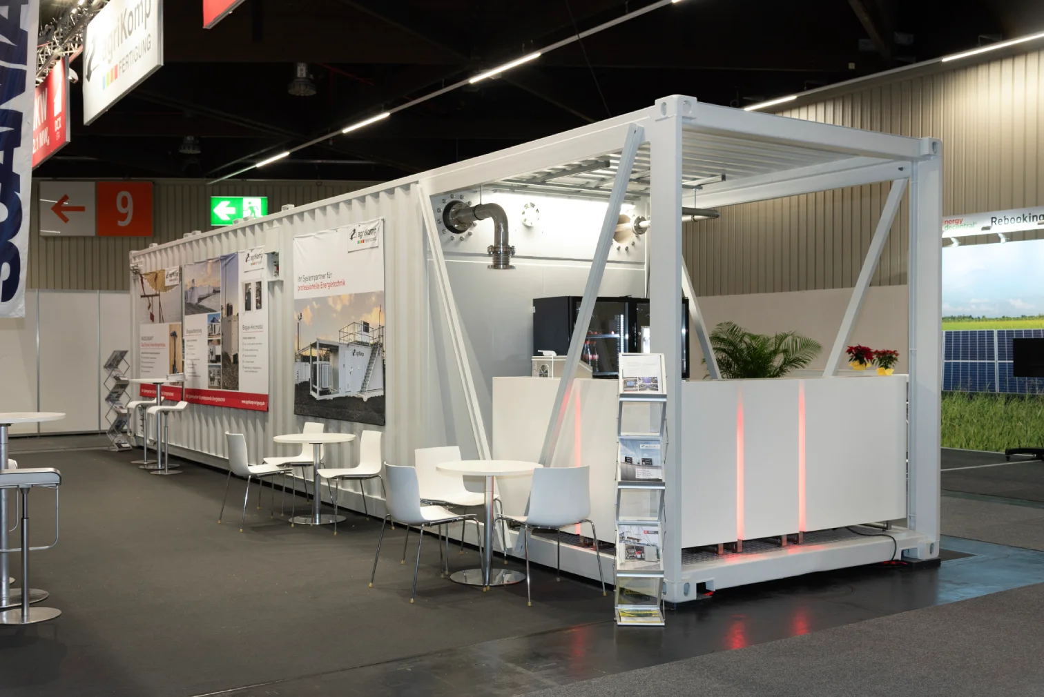 Weisser Container-Messestand von agriKomp mit Energietechnik-Banner, weissen Sitzgruppen und Prospektstaender nahe Halle 9 auf der Messe Nuernberg.