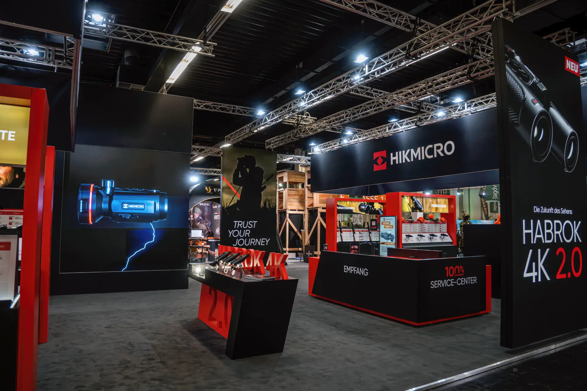 HIKMICRO-Messestand in Dortmund mit Empfangstheke, Service-Center und Produktwand zur Habrok 4K 2.0 sowie beleuchtetem Trust-Your-Journey-Display.