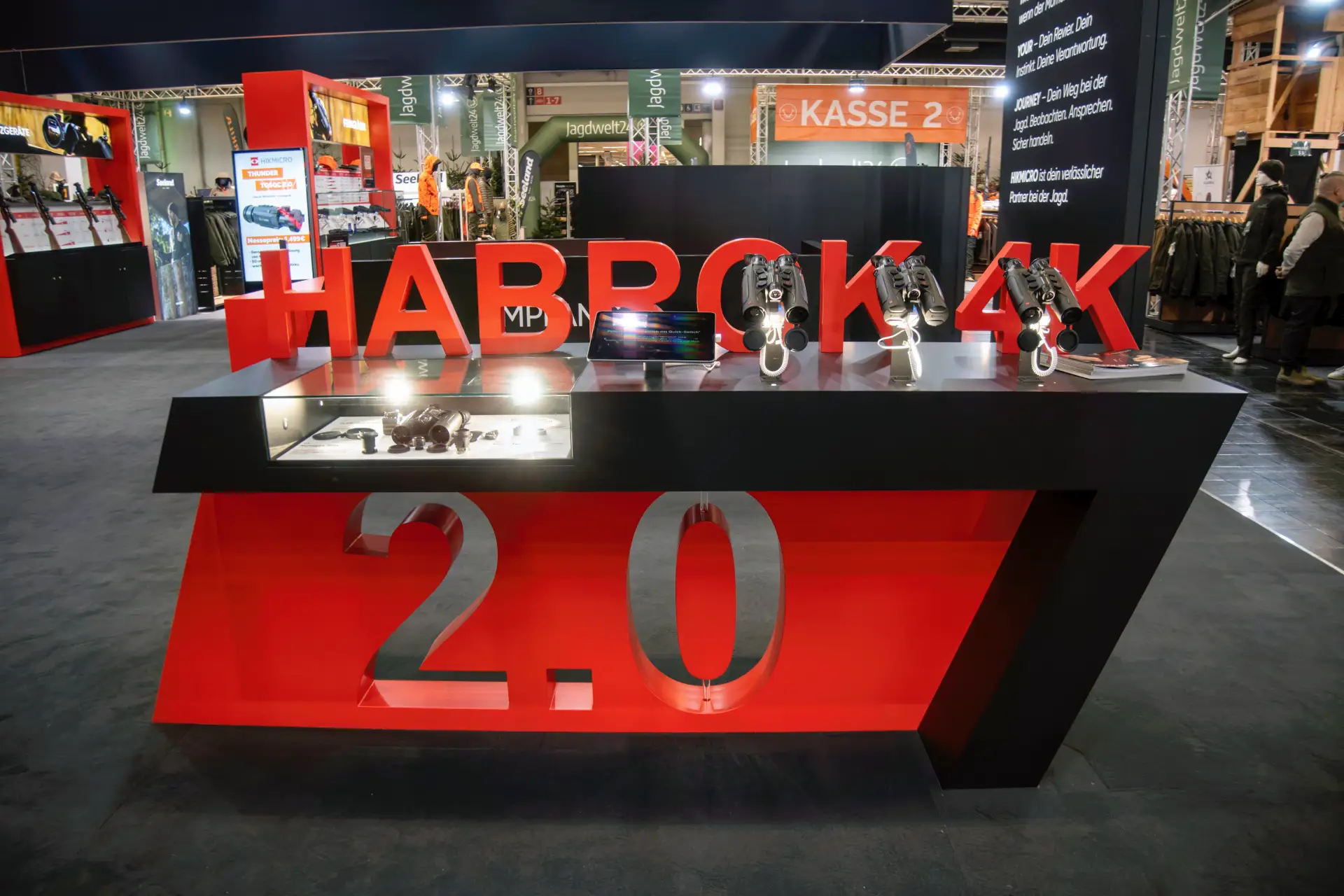 Roter Präsentationstresen am HIKMICRO-Messestand mit großem Schriftzug Habrok 4K 2.0 und ausgestellten Wärmebildgeräten unter Spotbeleuchtung.