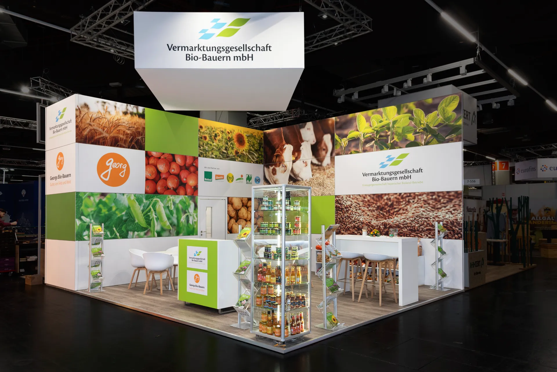 Farbenfroher Messestand der Vermarktungsgesellschaft Bio-Bauern mbH in Nürnberg mit Lebensmittel-Wandbildern, Produktregal und Sitzbereichen.