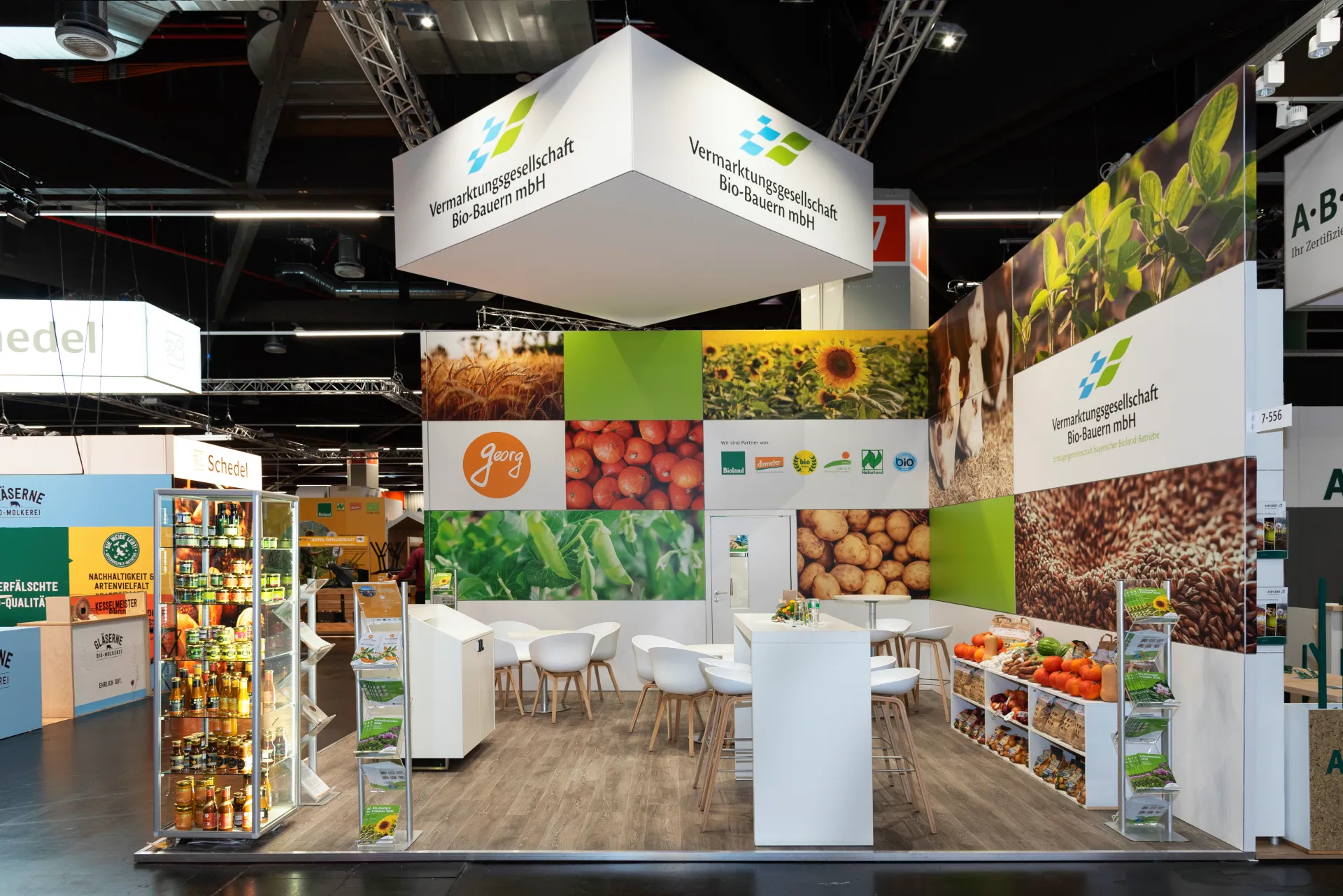 Messebau in Nürnberg für Bio-Bauern mbH mit beleuchteter Deckenkonstruktion, großflächiger Foto-Bildwand zu Bio-Lebensmitteln, Produktregalen und weißen Stehtischen.