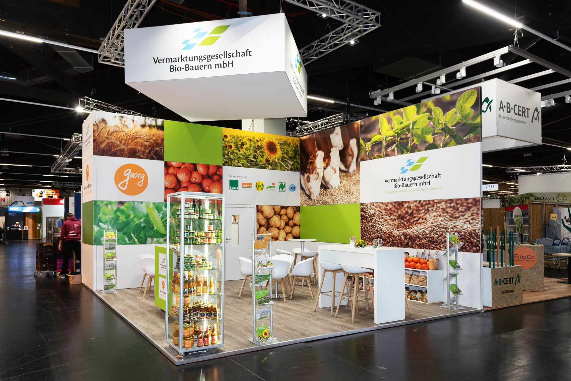 Frontansicht des Messestands der Vermarktungsgesellschaft Bio-Bauern mbH in Nürnberg mit Logo-Deckenbanner, Bildwand und offener Sitzbereich-Lounge.