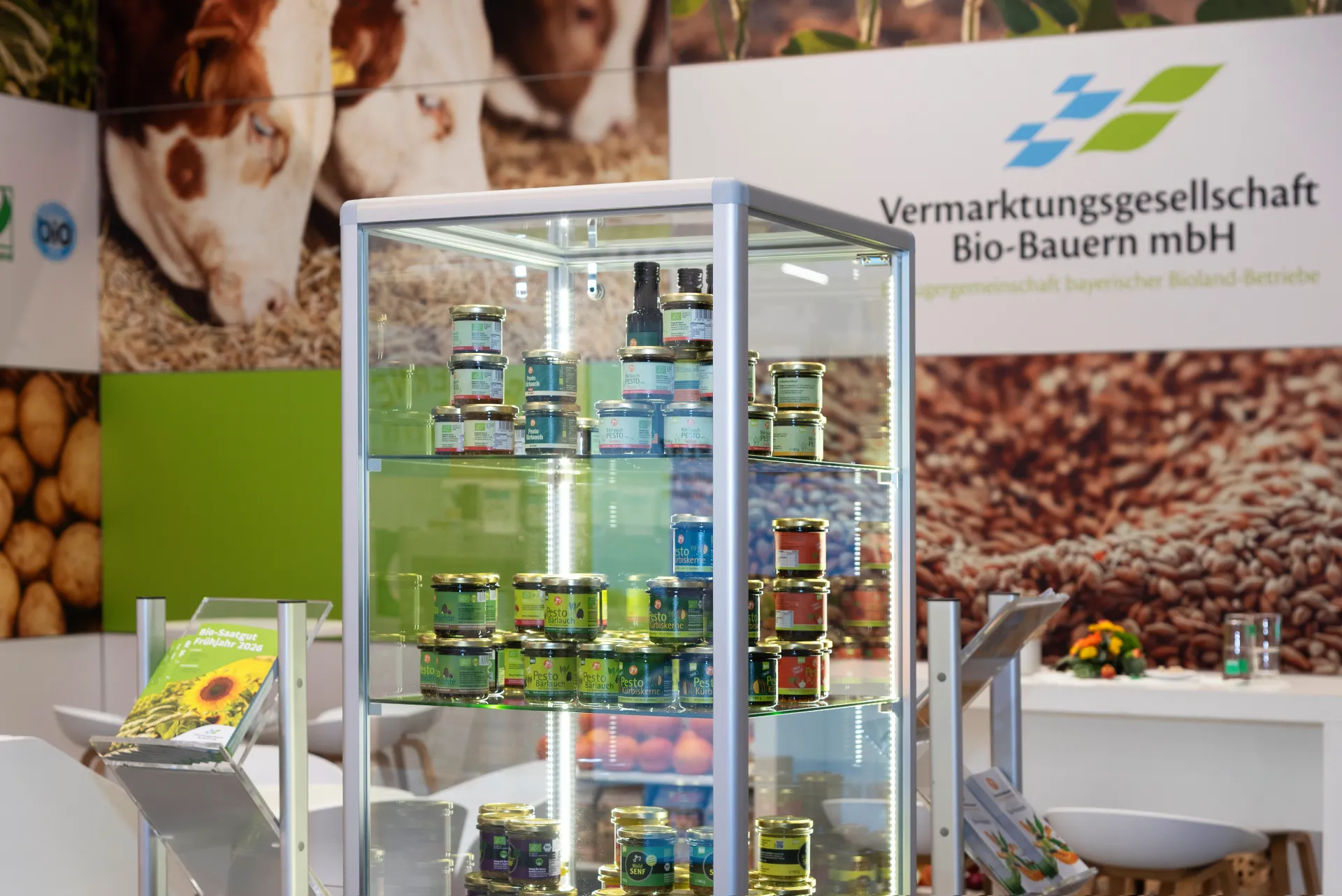 Beleuchtete Glasvitrine mit Bio-Gläsern am Messestand der Vermarktungsgesellschaft Bio-Bauern mbH in Nürnberg vor Logowand mit Tier- und Feldmotiven.