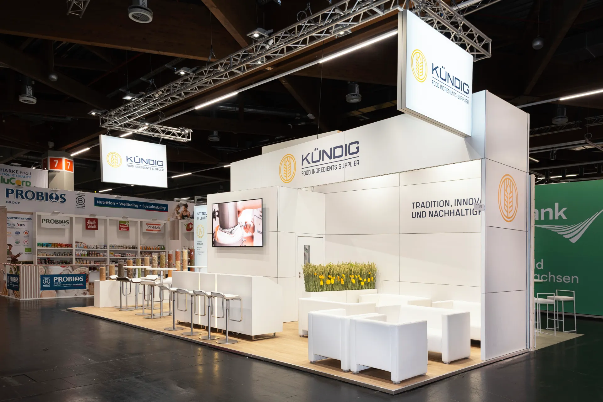Heller Messestand von Kündig in Nürnberg mit Slogan Tradition, Innovation und Nachhaltigkeit, beleuchteten Logo-Bannern, Bildschirm und weißer Loungemöblierung.