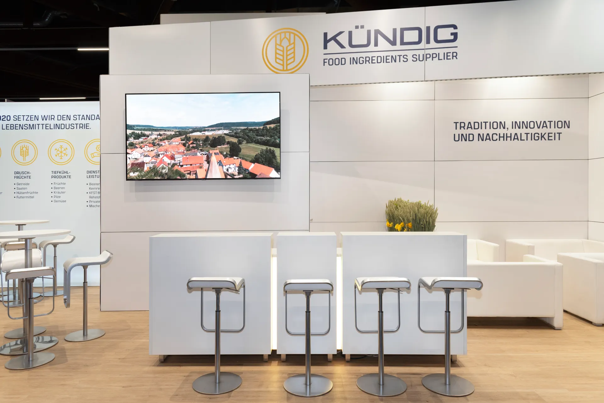 Bartheke mit Hockern am Kündig-Messestand in Nürnberg, mit Monitor, Logo Food Ingredients Supplier und beschrifteter Produktwand.