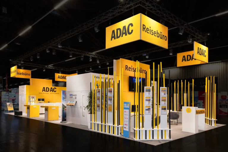 Großer gelb-schwarzer ADAC-Reisebüro-Messestand auf der Freizeitmesse Nürnberg mit beleuchteten Logo-Deckenbannern, Beratungstheken und Prospektständern.