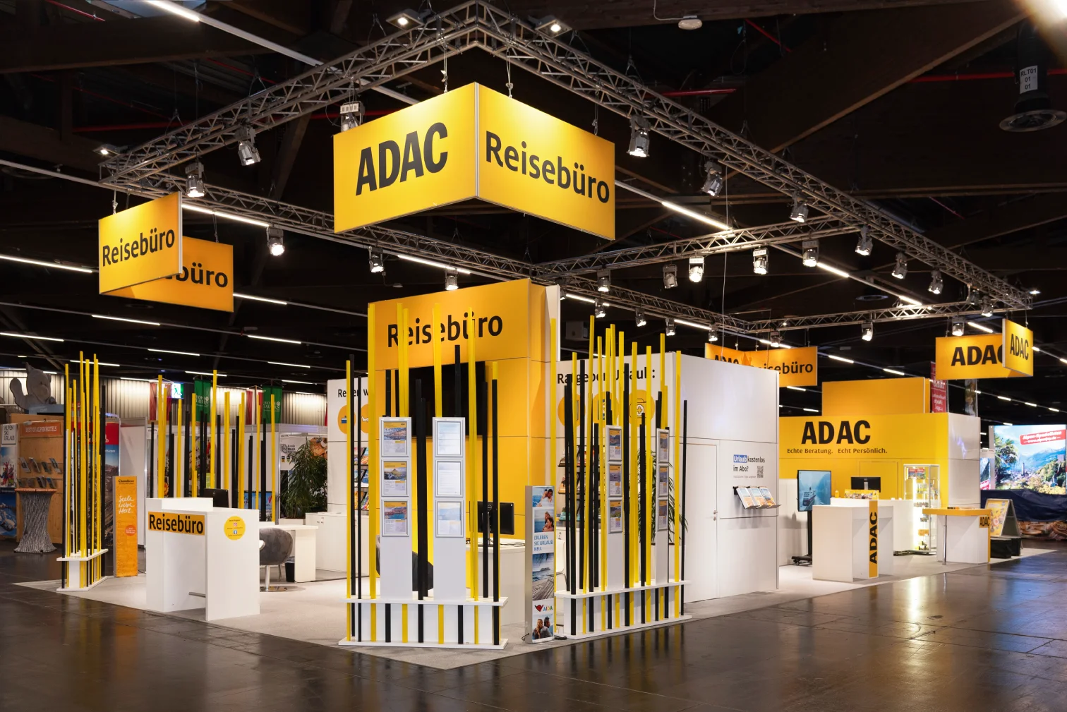 Eckiger ADAC-Reisebüro-Messestand auf der Freizeitmesse Nürnberg mit beleuchtetem Traversen-Deckenbanner und gelb-schwarzen Stelen.