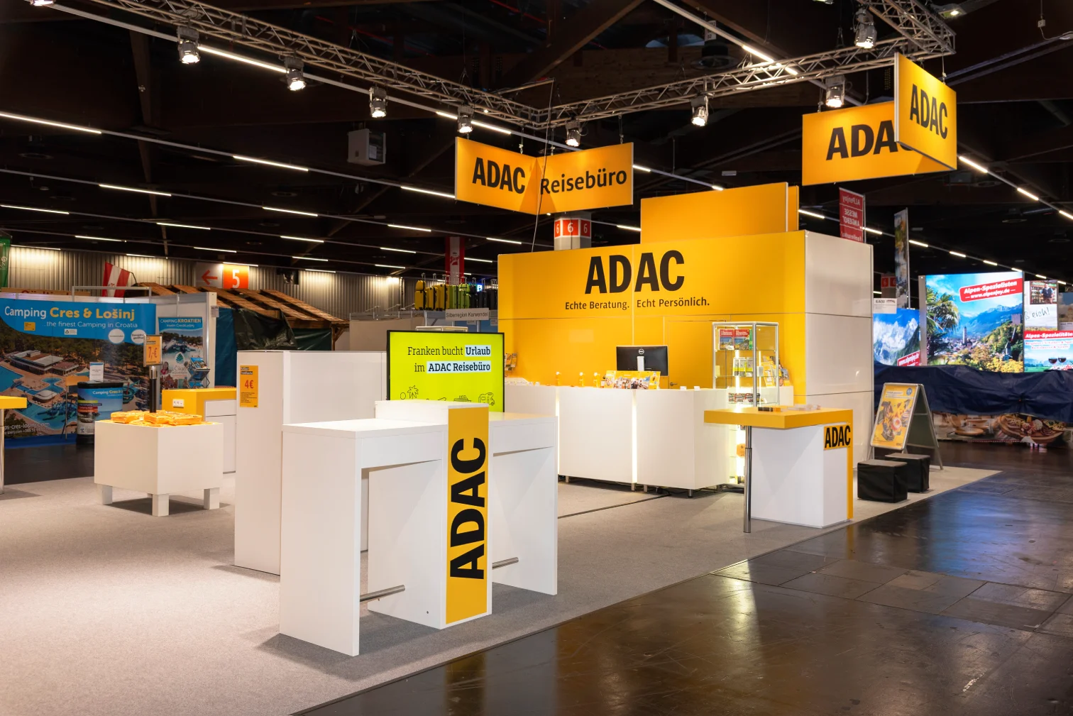 ADAC-Reisebüro-Messestand auf der Freizeitmesse Nürnberg mit gelber Theke, Slogan Echte Beratung Echt Persönlich und weißen Beratungstresen.