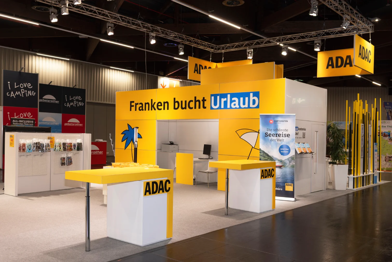 ADAC Reisebüro-Messestand auf der Freizeitmesse Nürnberg mit gelbem Tresen, Prospektregalen und Slogan Franken bucht Urlaub samt Palmen-Logo.