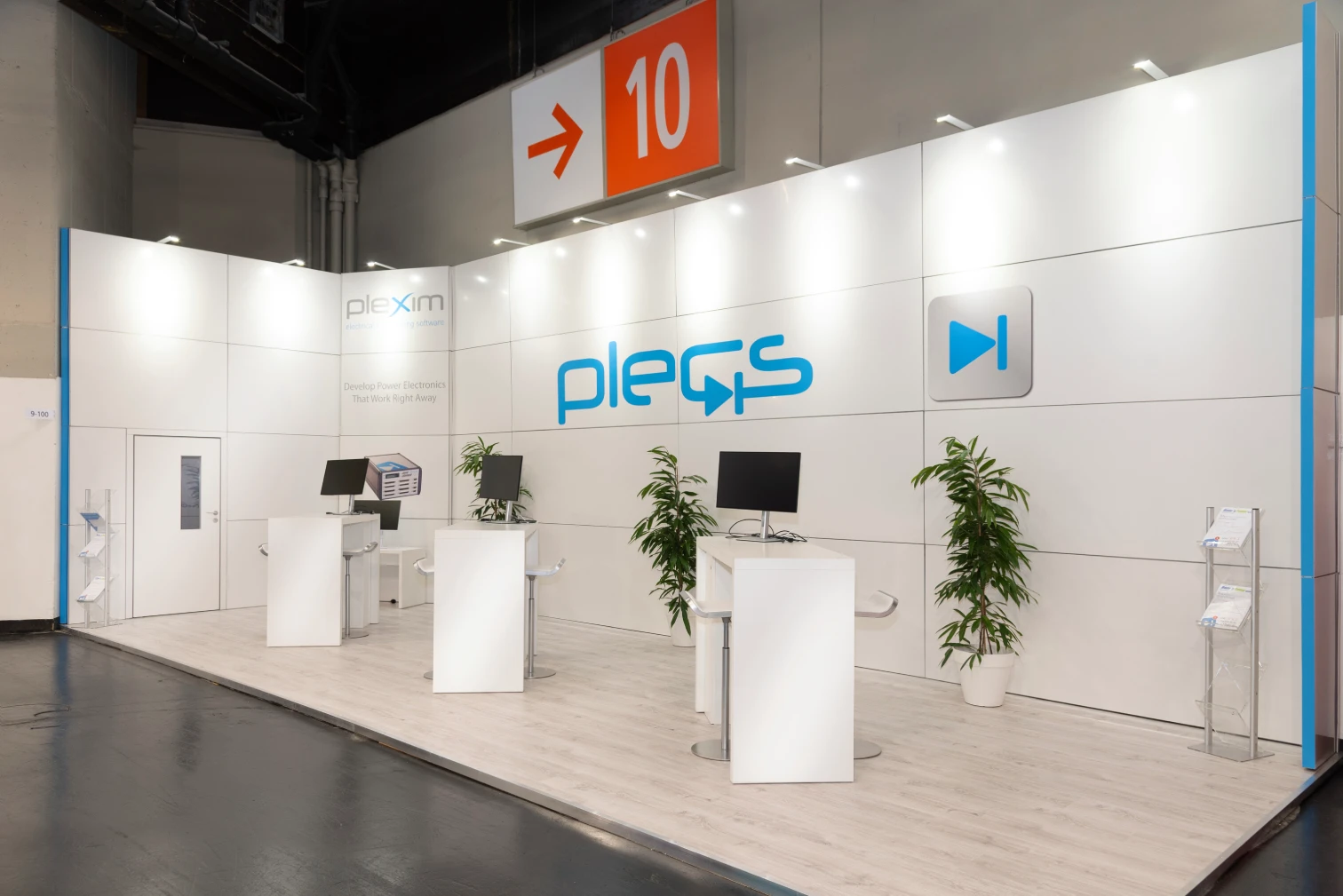 Heller offener Messestand der Plexim GmbH mit Plecs-Logo, Theken, Monitoren und Pflanzen unter dem Hallenschild 10 auf der PCIM Nürnberg.