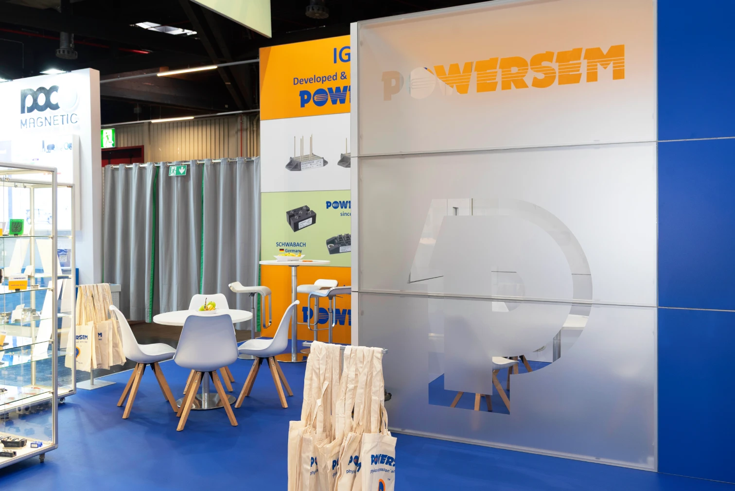 Messestand der Powersem GmbH auf der PCIM Nuernberg mit satinierter POWERSEM-Wand, blauem Boden, weisser Sitzgruppe und Stoffbeuteln.