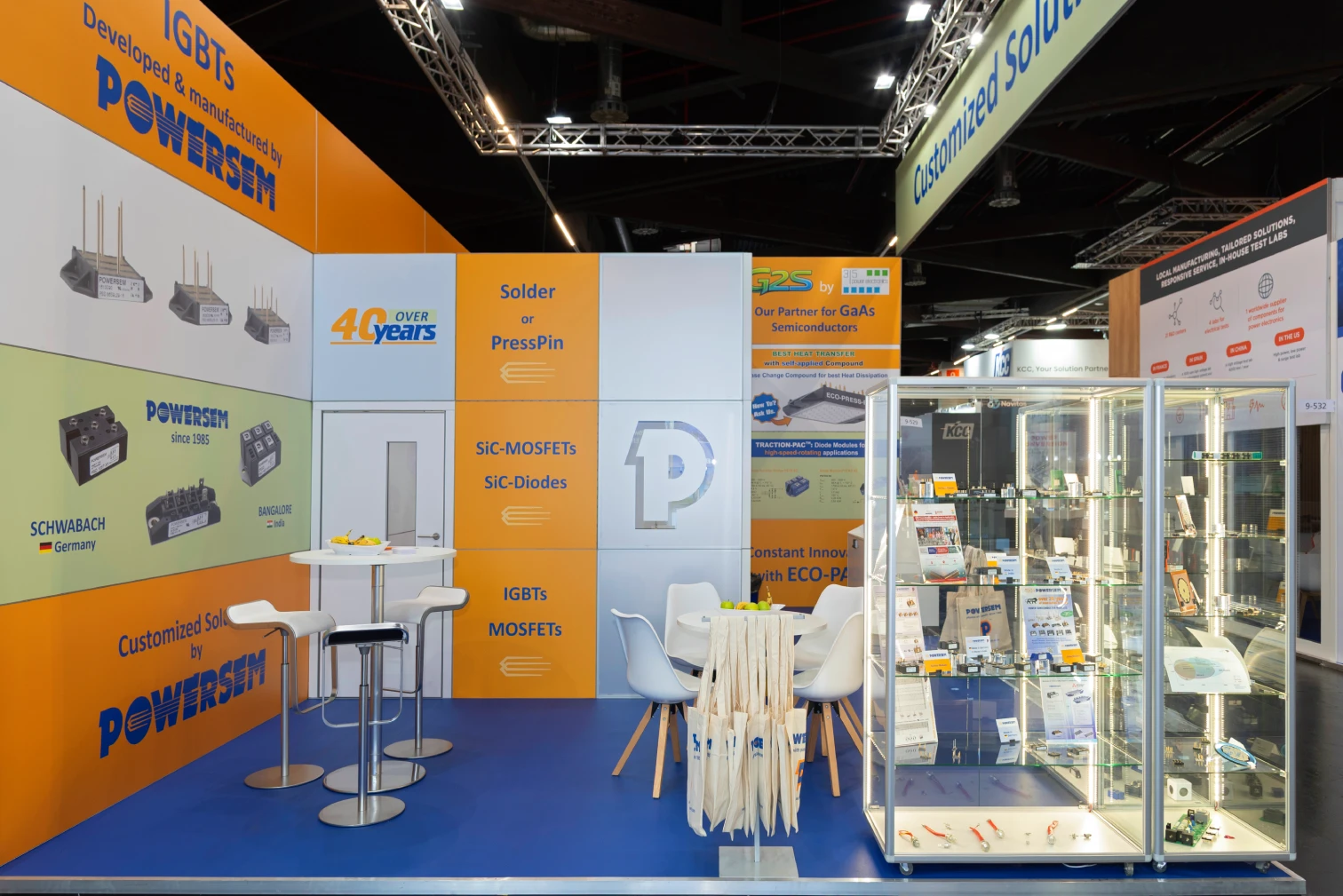Innenansicht des Powersem-Messestands auf der PCIM in Nürnberg mit Barhockern, weißen Stühlen, Produktwand zu SiC-MOSFETs und IGBTs sowie beleuchteter Vitrine mit Bauteilen.
